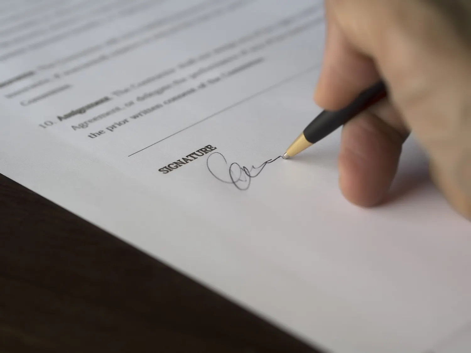 Una mano firma un contrato con un bolígrafo sobre una mesa de madera