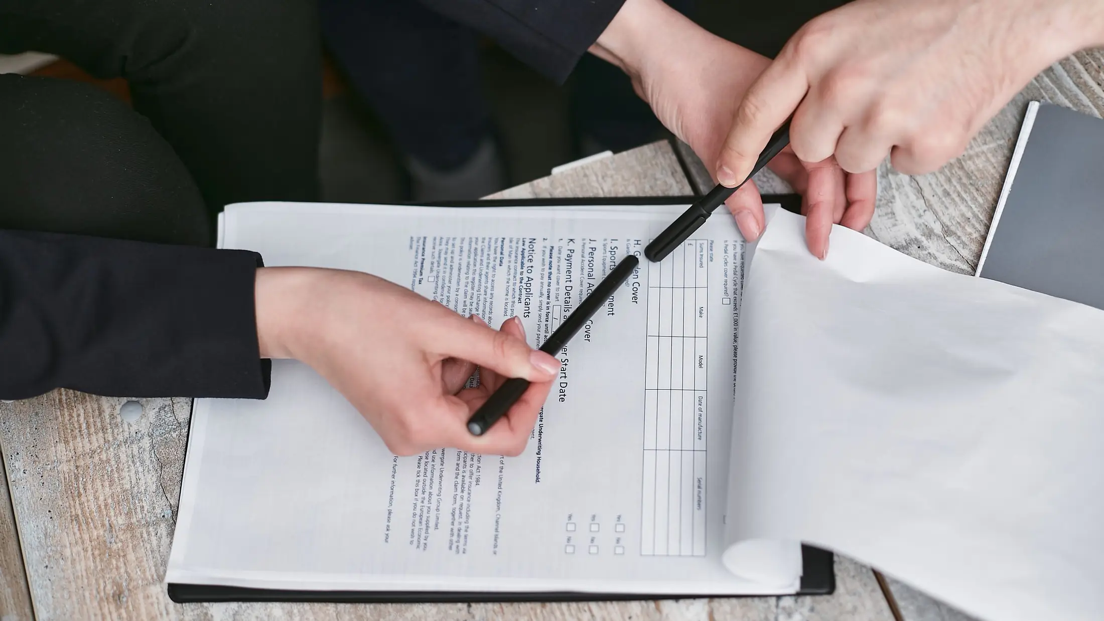 Dos personas repasando con un bolígrafo las cláusulas de un documento sobre la mesa
