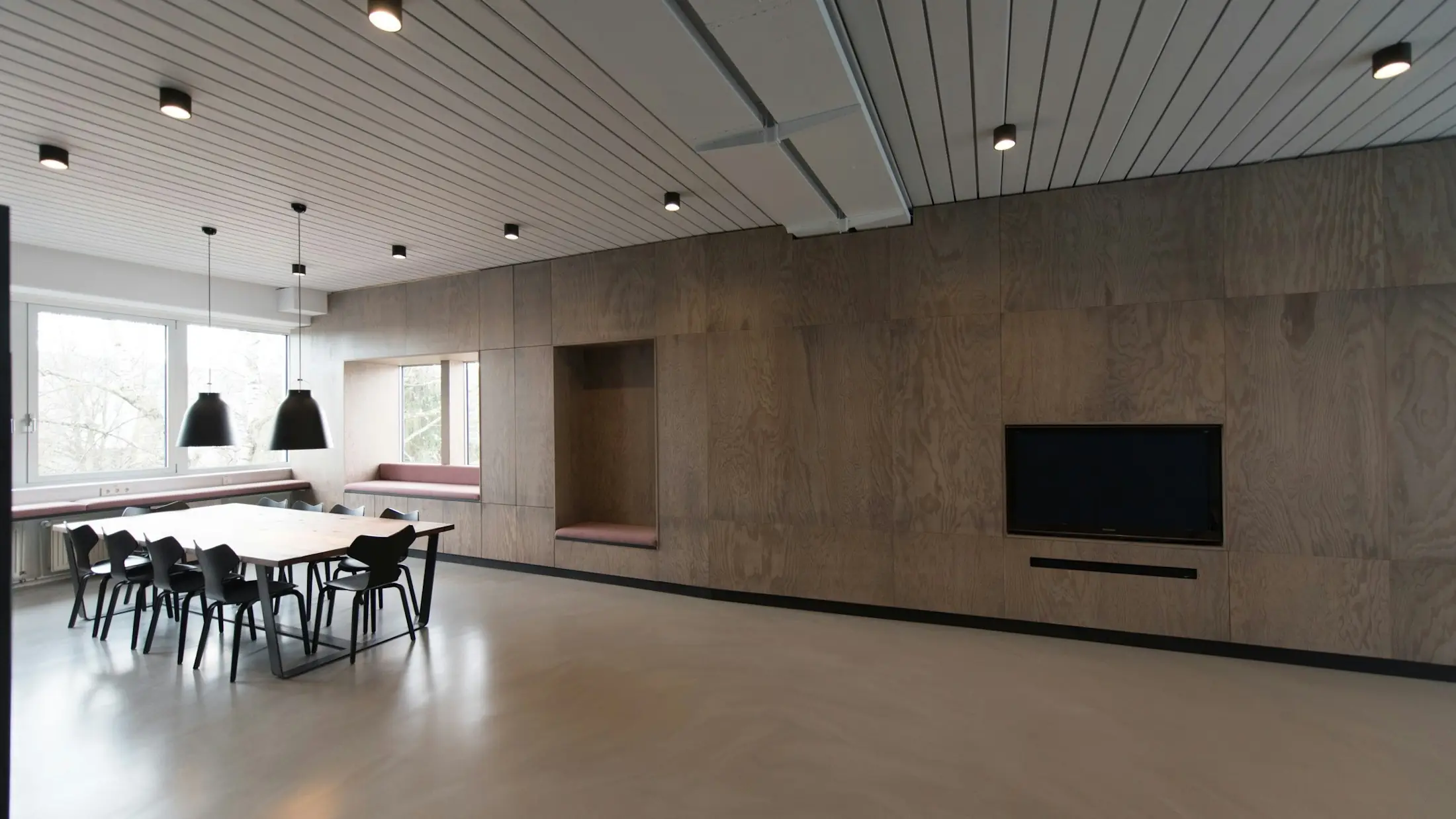 Sala de reuniones revestida de madera, con mesa larga, lámparas colgantes y un banco junto a la ventana