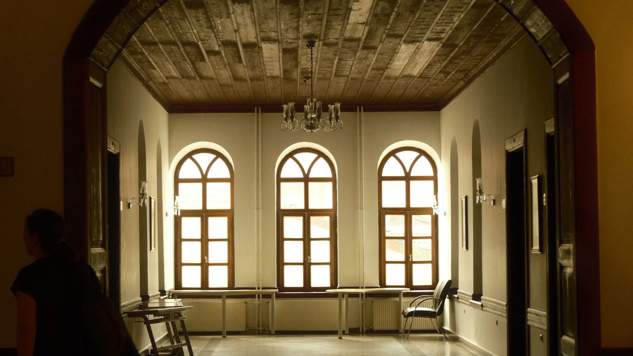 Sala vacía de un edificio institucional con ventanales en arco y bancos de madera